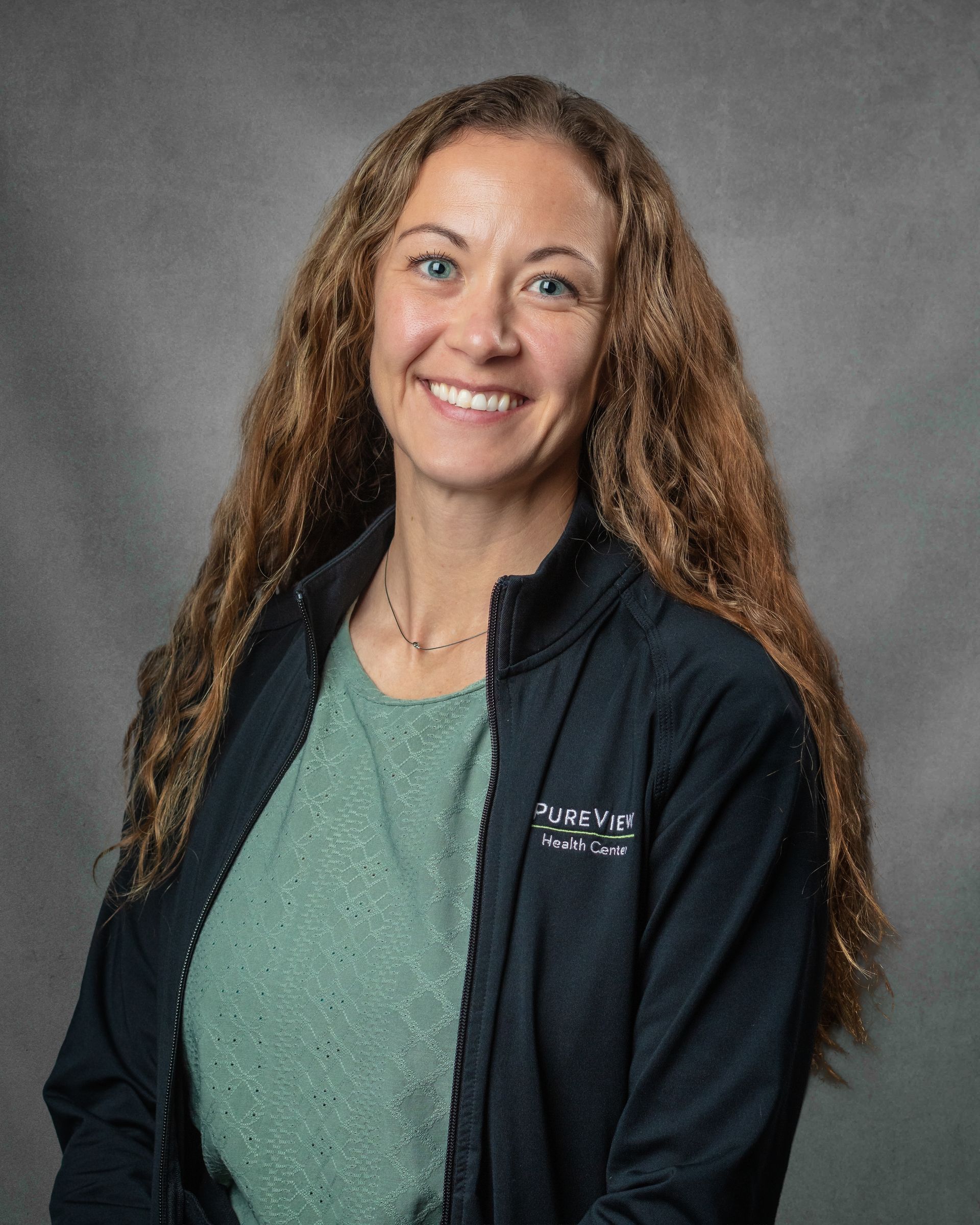 A woman in a green shirt and black jacket is smiling for the camera.