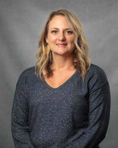 A woman in a gray sweater is smiling for the camera.
