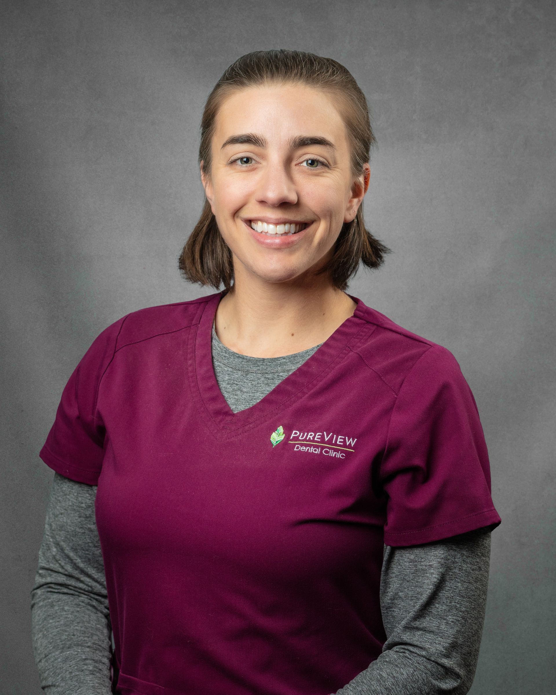 A woman is purple scrubs is smiling.