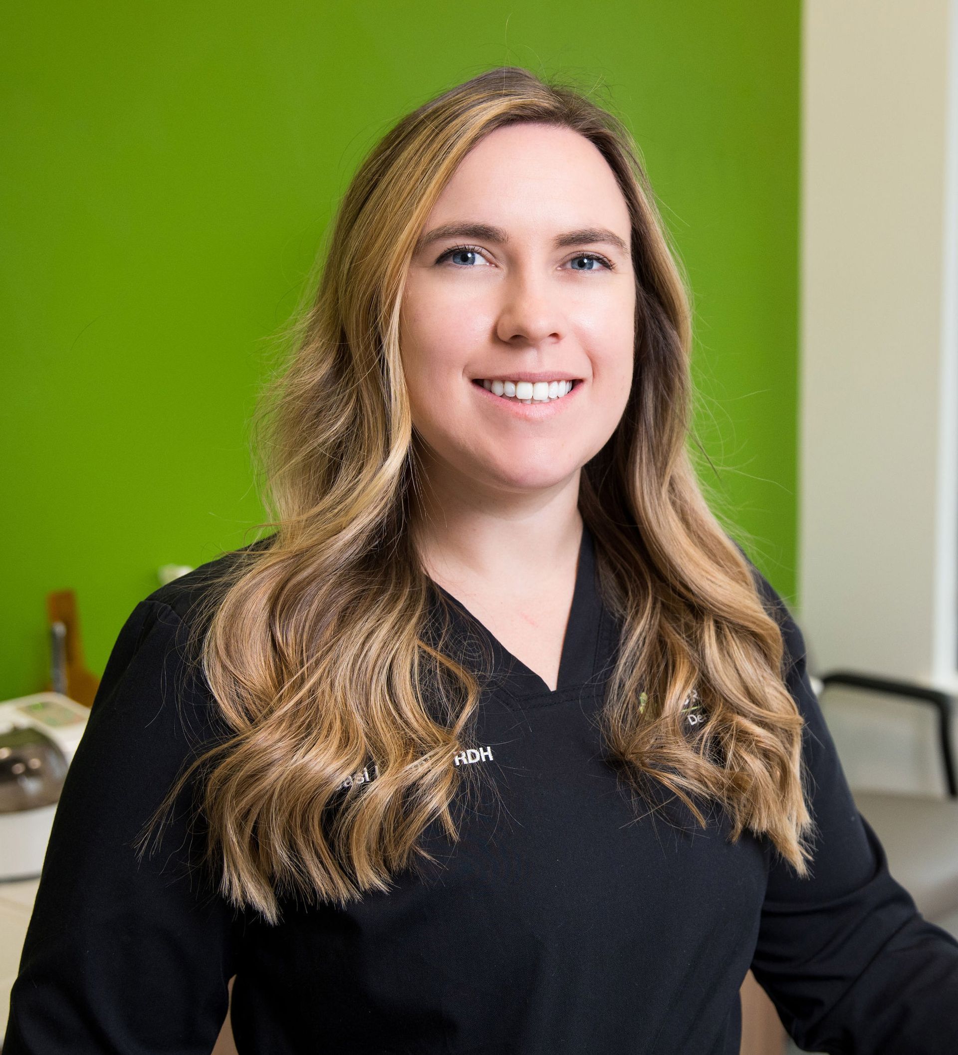 A woman in a black shirt is smiling in front of a green wall.