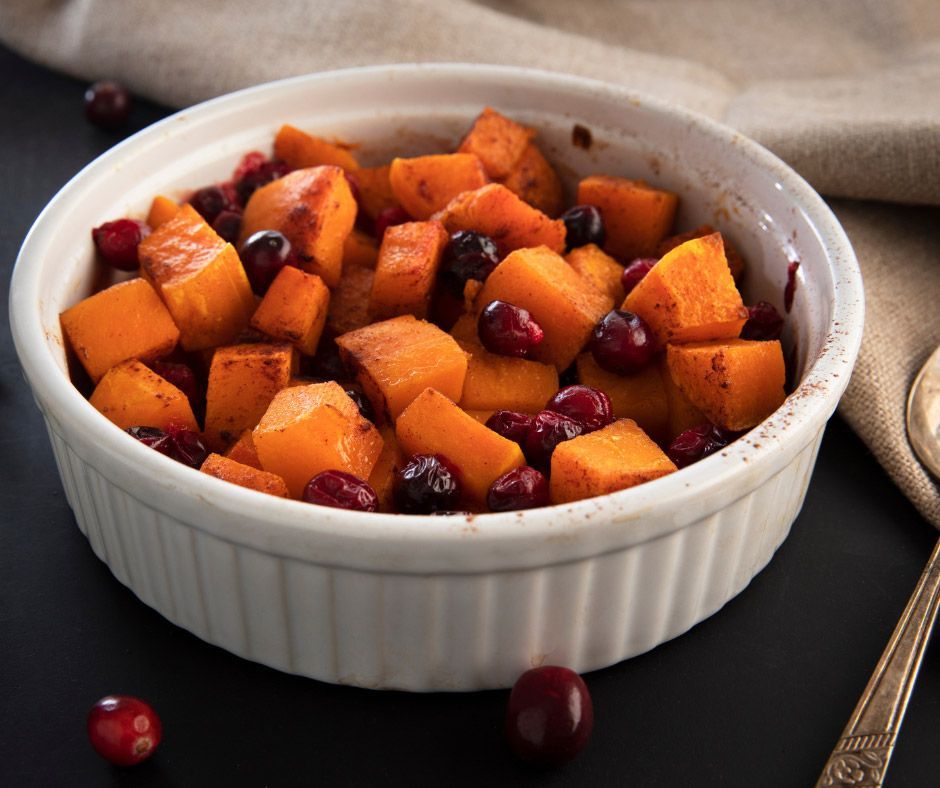 A bowl of butternut squash and cranberries with a spoon on a table.