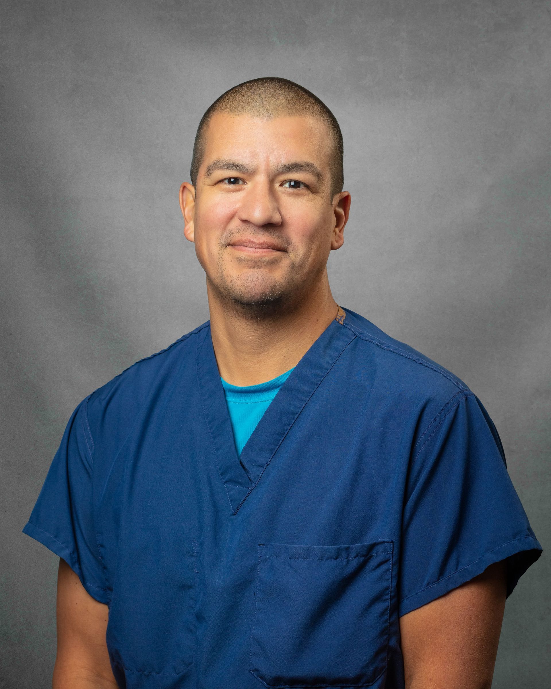 A man wearing blue scrubs is smiling for the camera..
