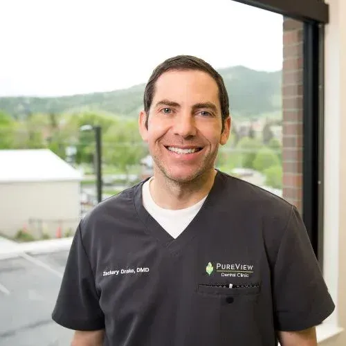 A man in a scrub top is smiling in front of a window.