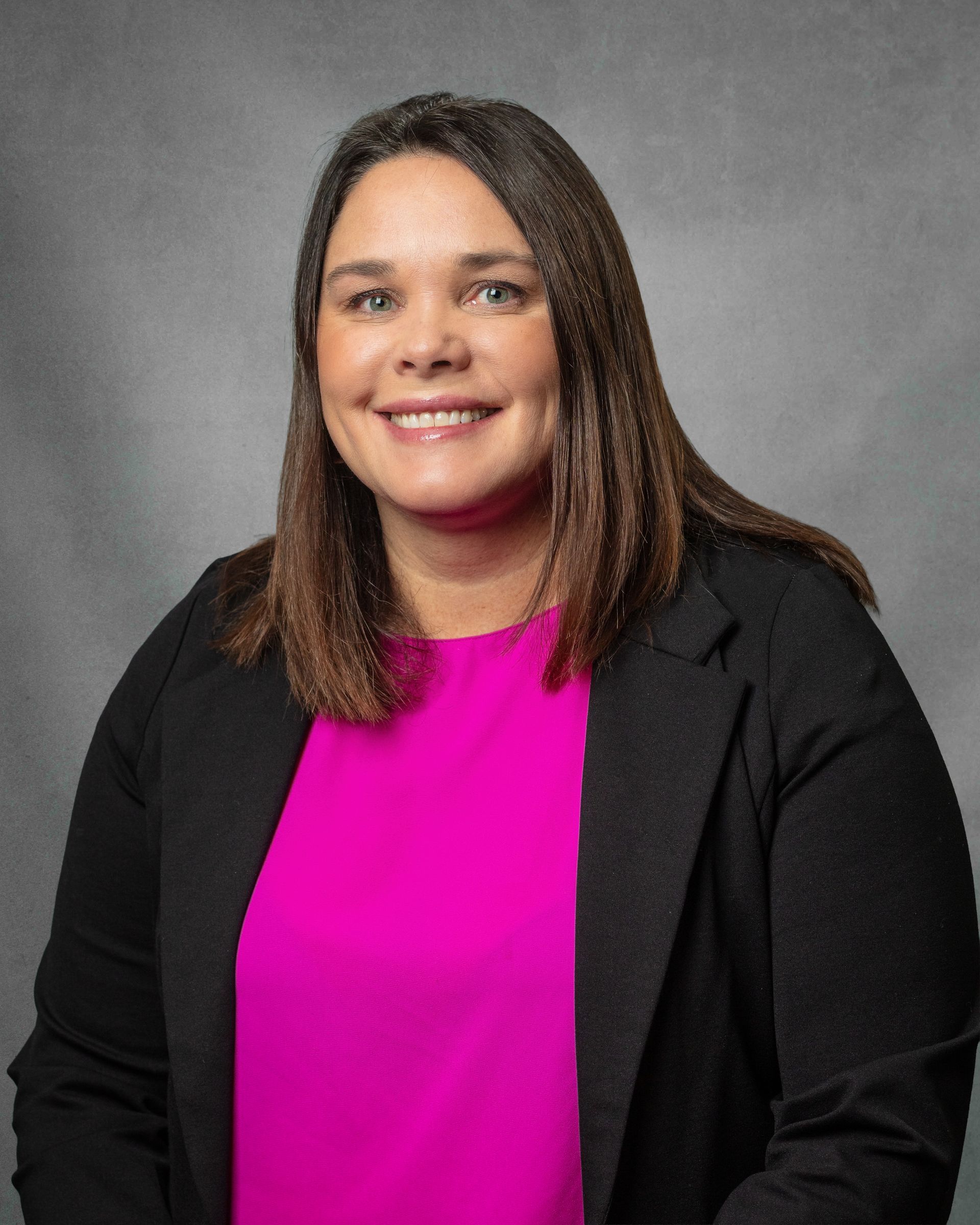 A woman wearing a pink shirt and black jacket is smiling for the camera.
