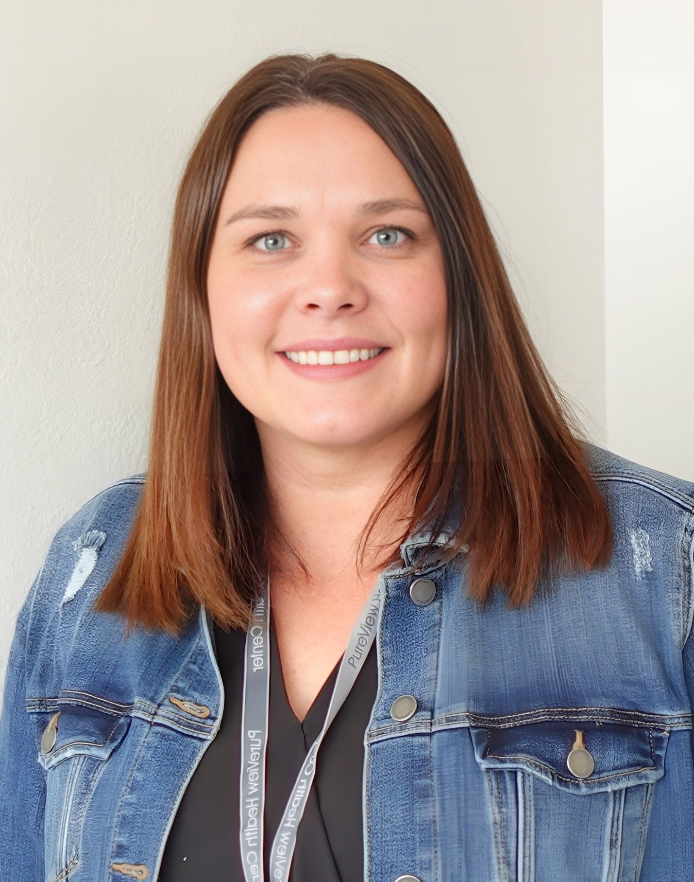 A woman wearing a denim jacket is smiling for the camera.