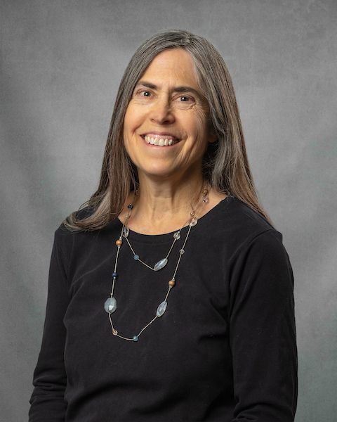 A woman in a black shirt with a long necklace is smiling for the camera.