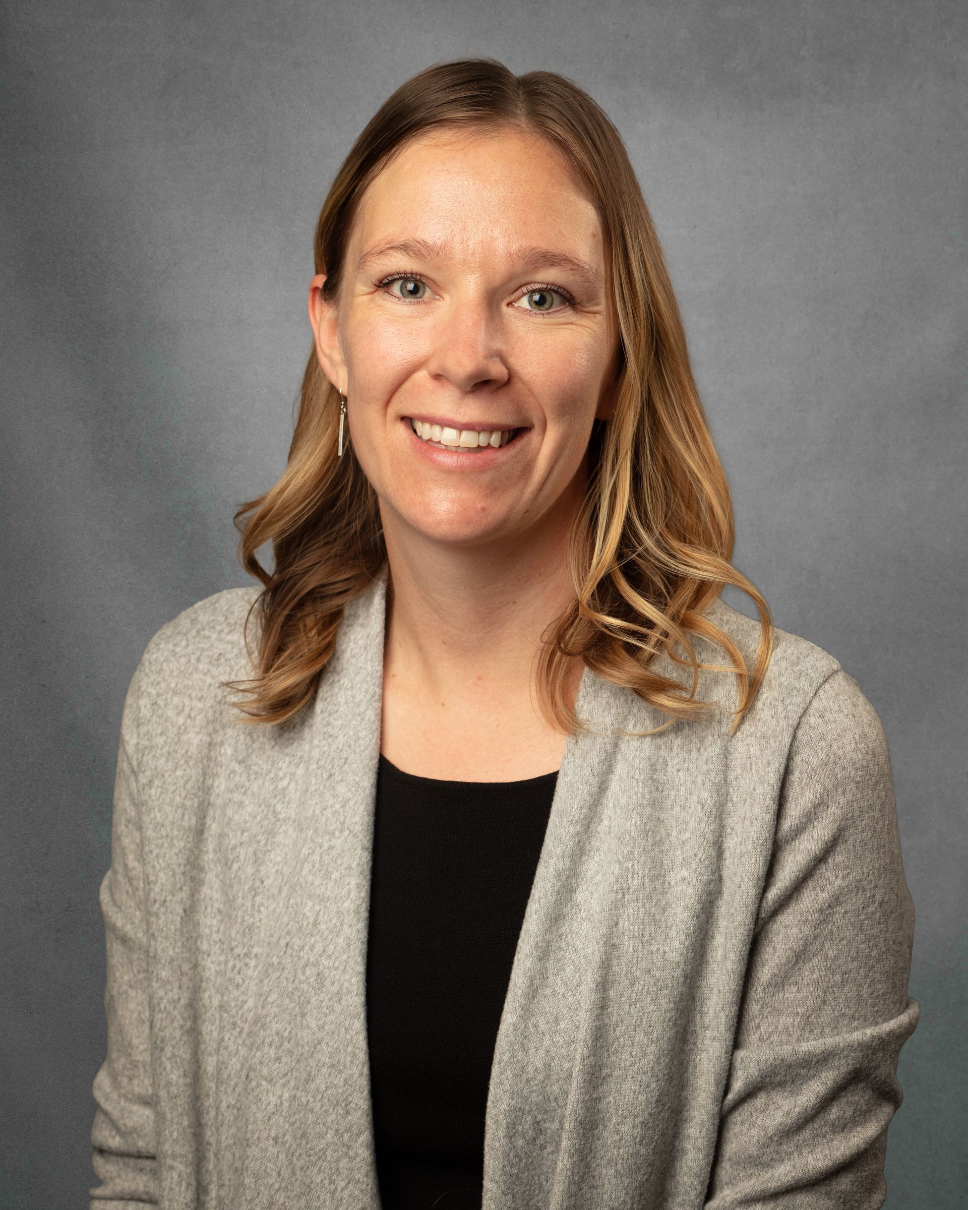 A womanwearing a tan cardigan is smiling at the camera. 