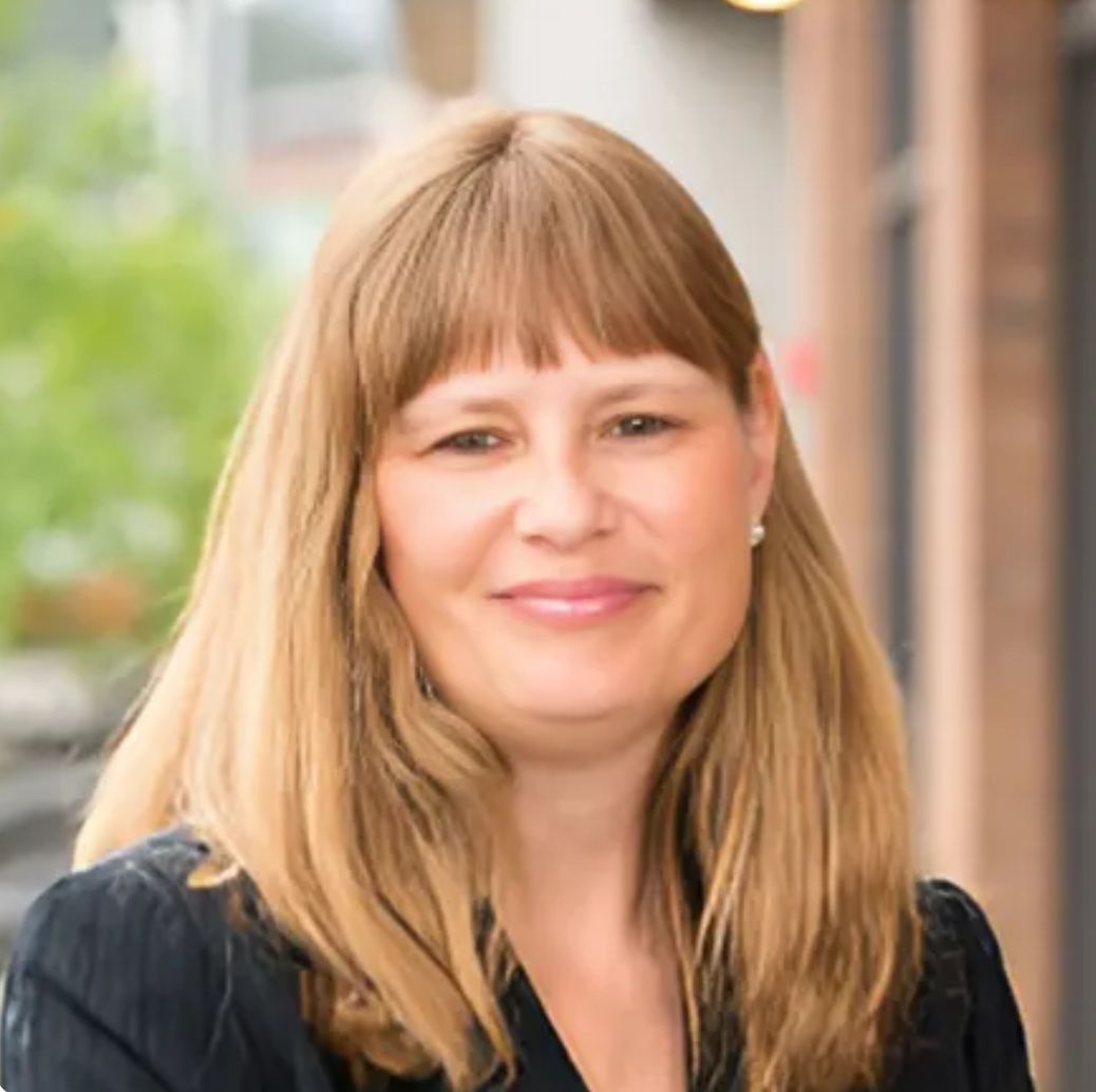 A woman with red curly hair and freckles is smiling for the camera.