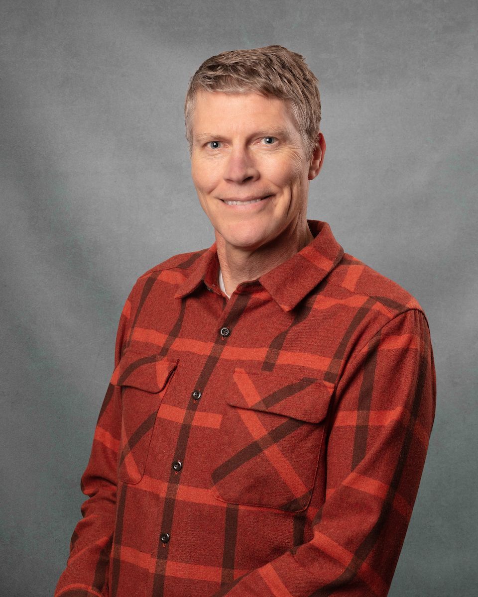 A man wearing an red flannel is smiling for the camera