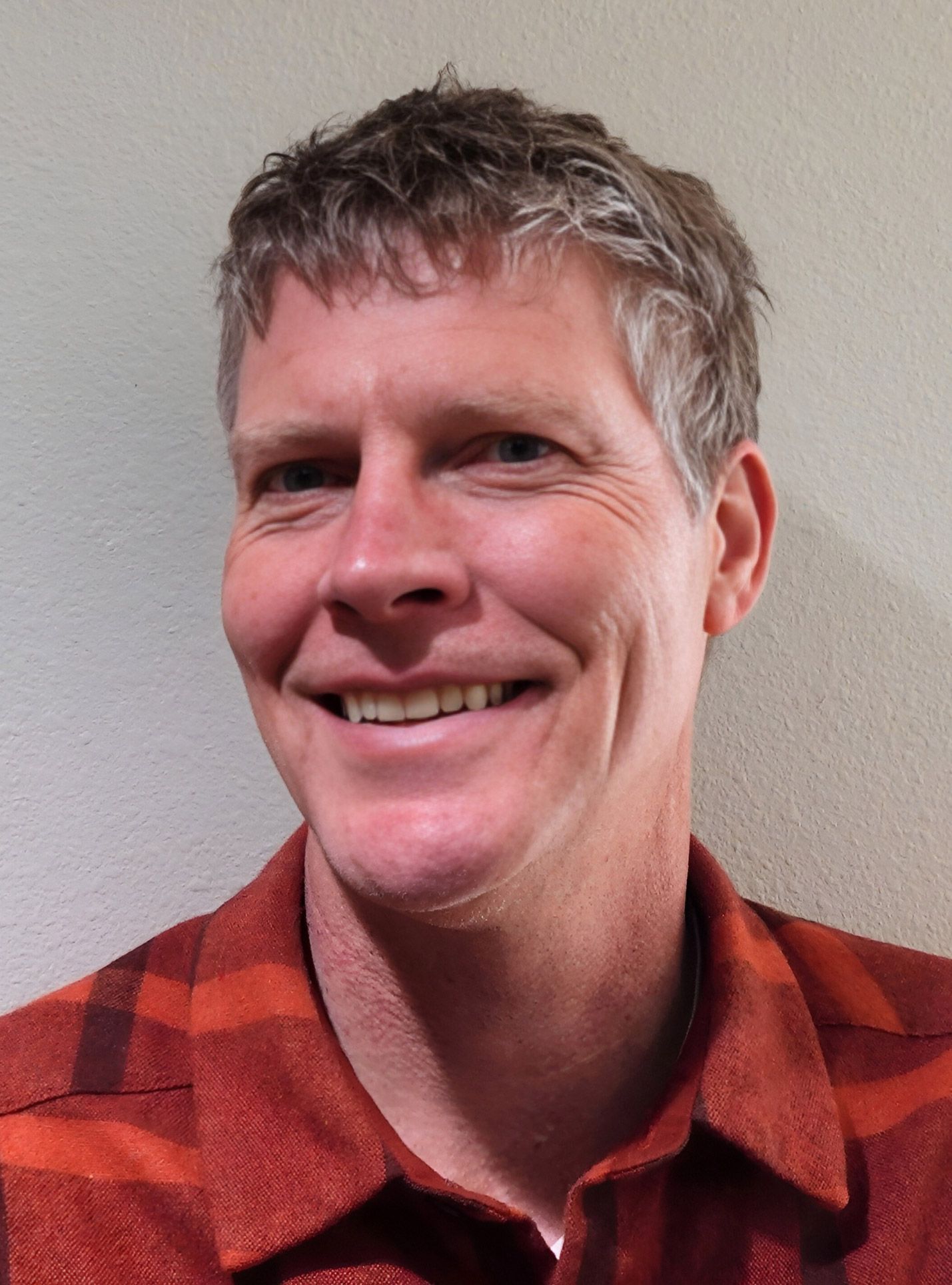 A man wearing an orange plaid shirt is smiling for the camera