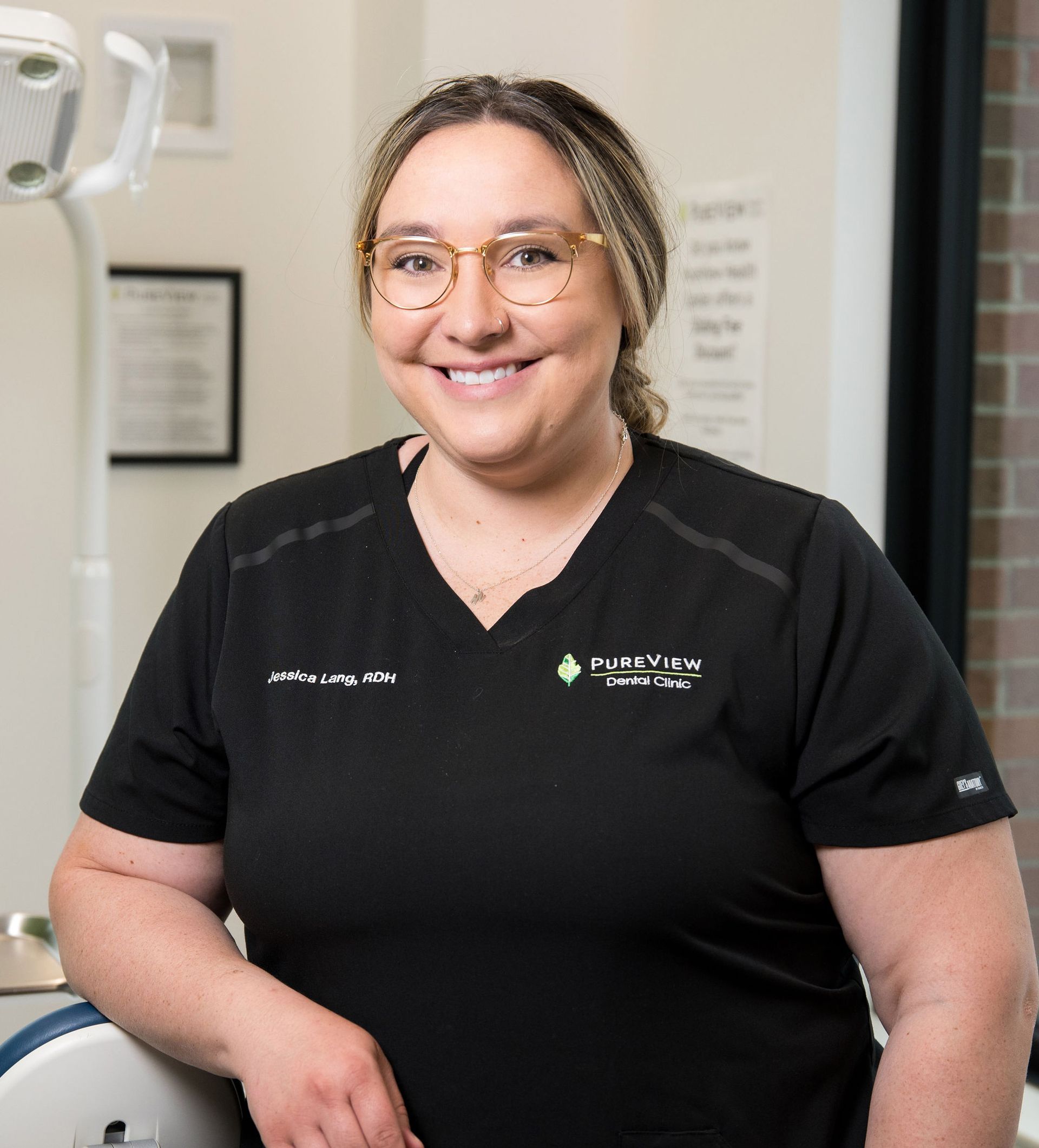 A woman wearing glasses and a black shirt is smiling in a dental office