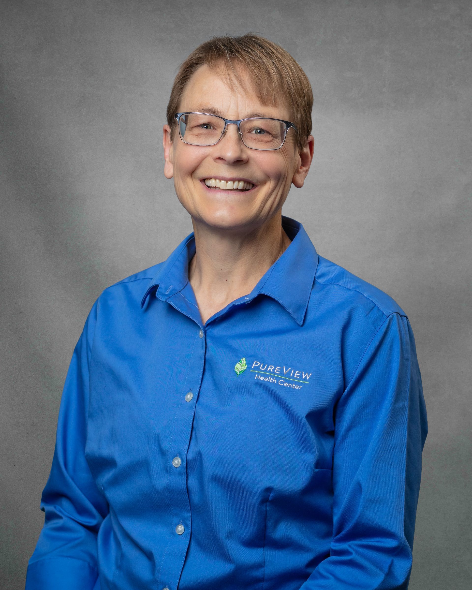 A woman with short hair in a blue button down smiling.