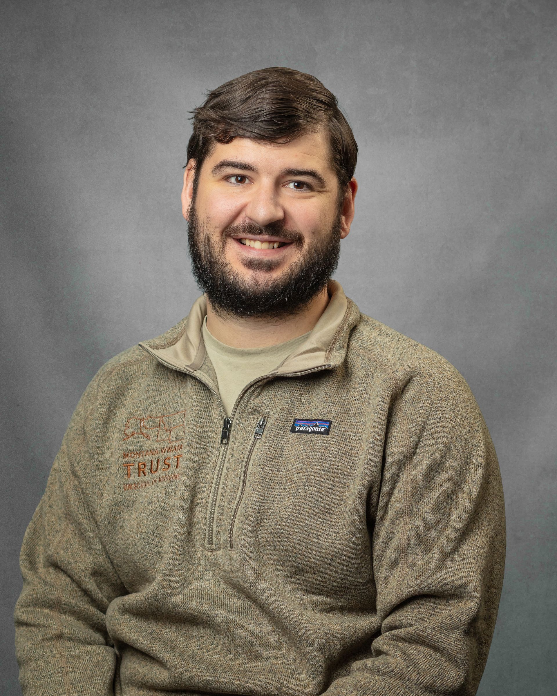 A man with a beard is wearing a tan quater-zip and smiling.