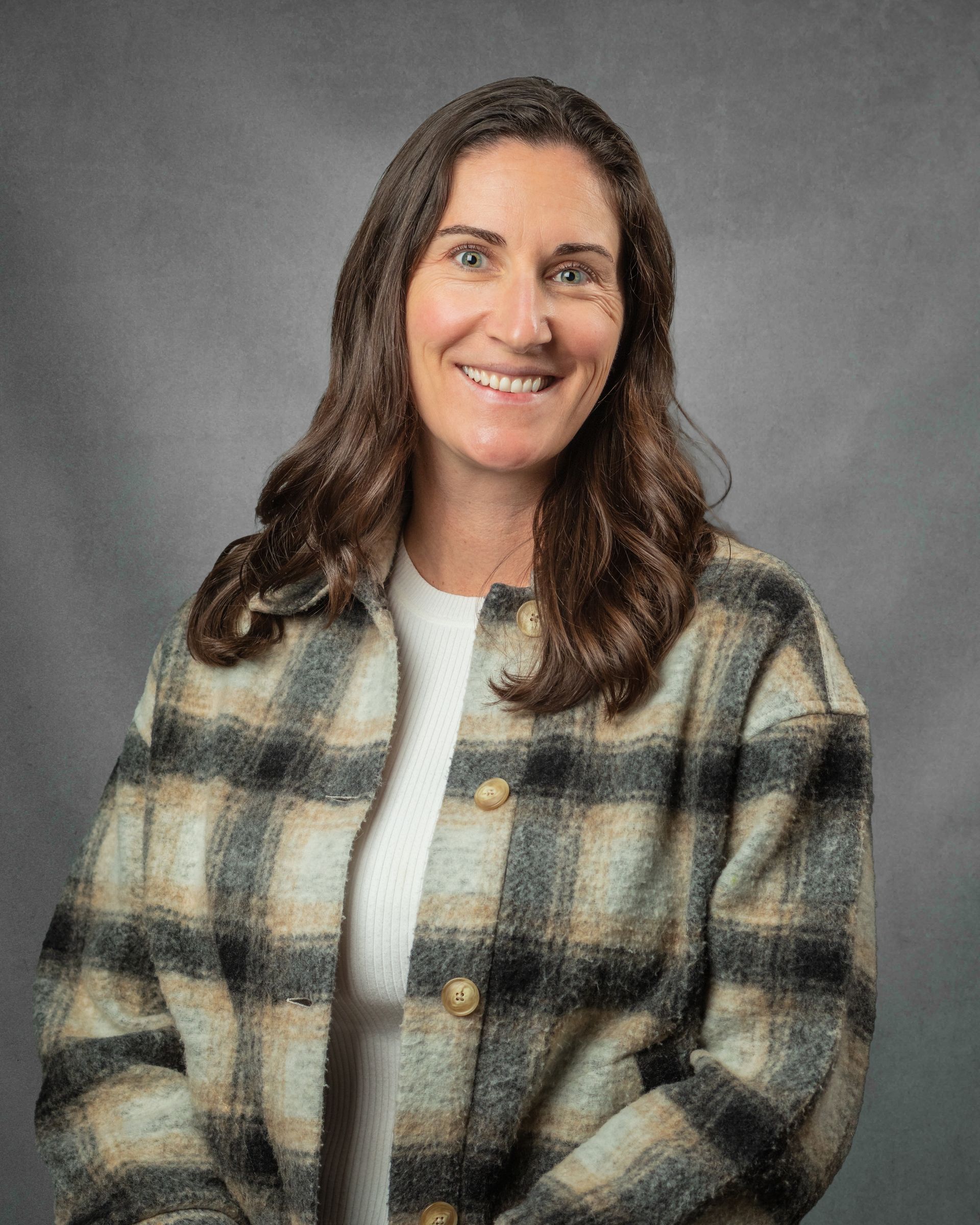 A woman wearing a blue sweater and earrings is smiling for the camera.