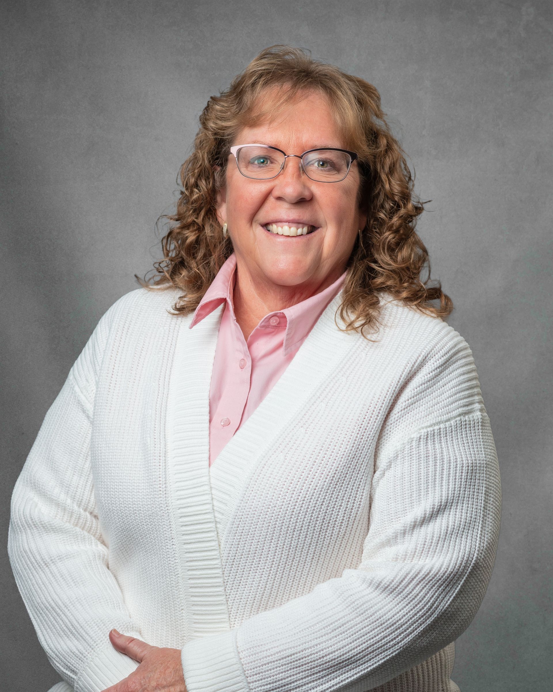 A woman in a purple shirt is standing in a field with her arms crossed and smiling.
