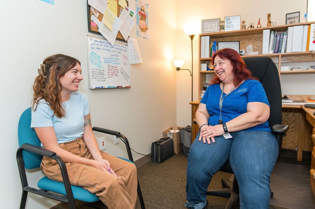 Two women are sitting in chairs talking to each other in a room.