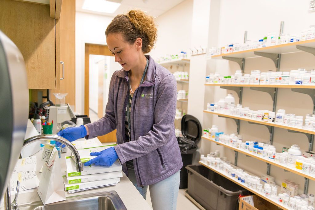 A woman is washing bottles in a sink in a pharmacy.
