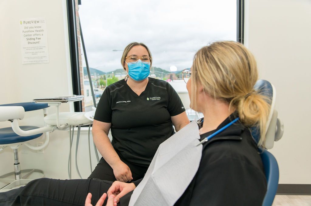 A woman is sitting in a dental chair talking to a dentist.