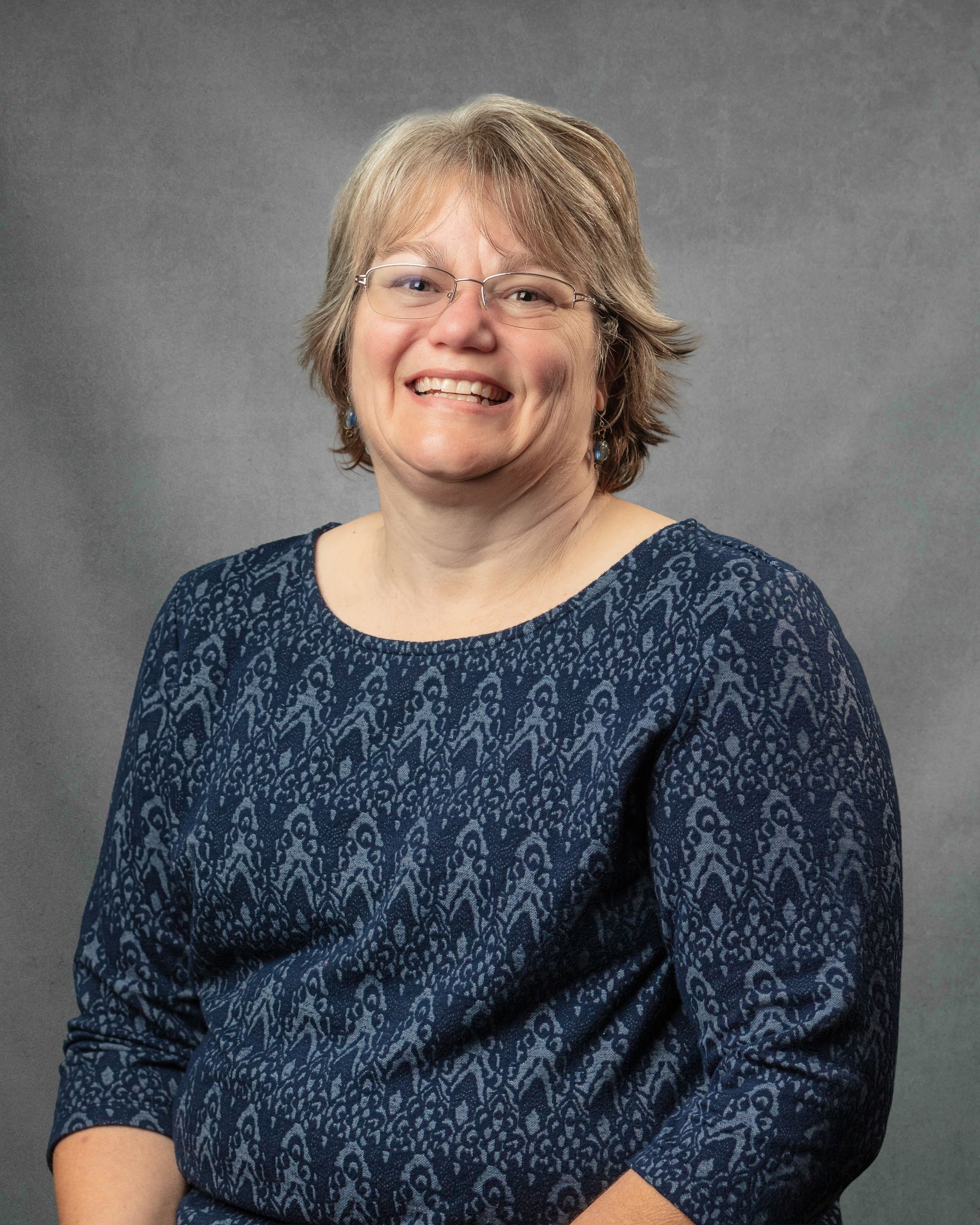 A woman with short hair in a blue top smiling at the camera.