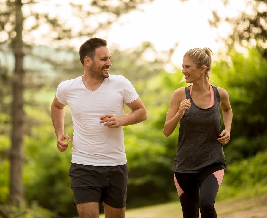 A man and a woman are jogging in the woods.