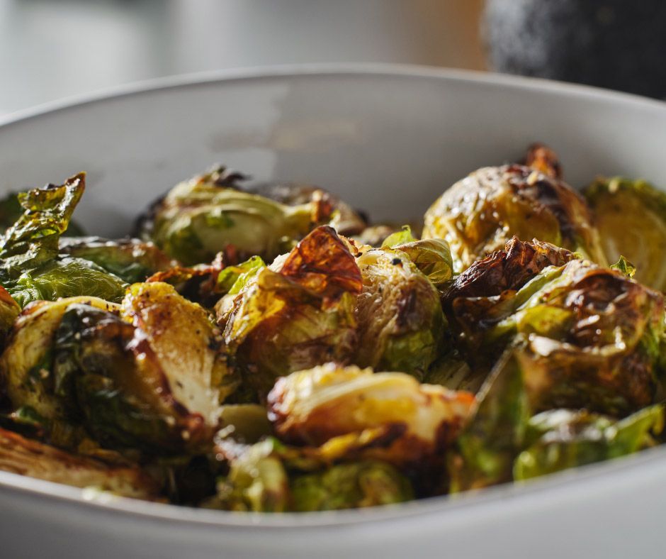 A close up of a bowl of roasted brussels sprouts on a table.