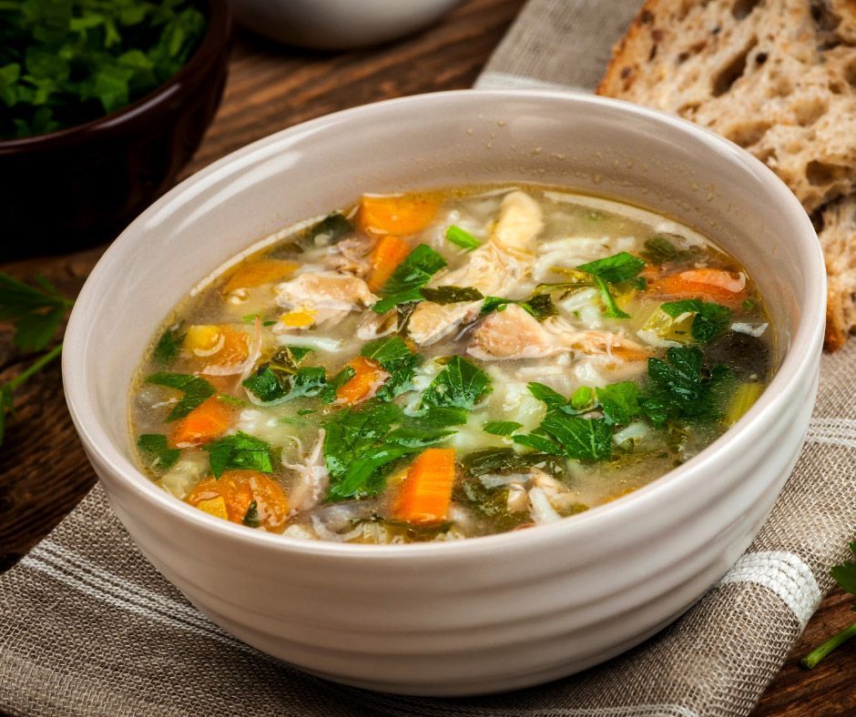 A bowl of chicken noodle soup with carrots and spinach on a table.