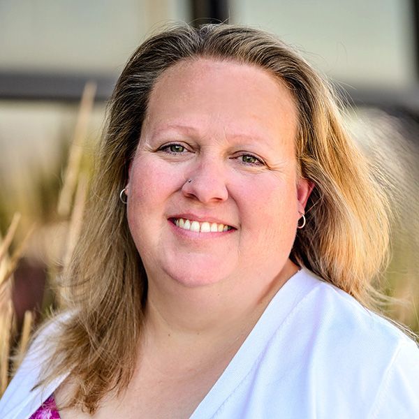 A woman in a grey shirt is smiling for the camera.