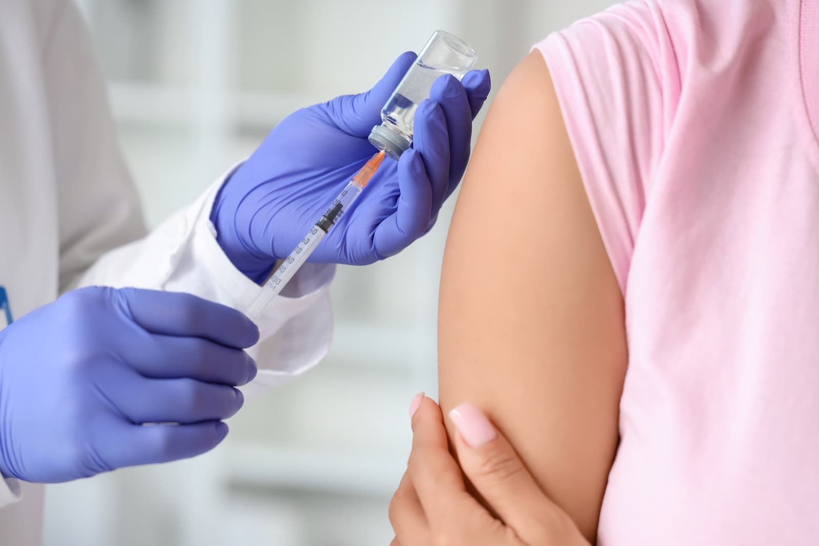 Healthcare professional wearing purple gloves preparing to administer a vaccine injection into a pat