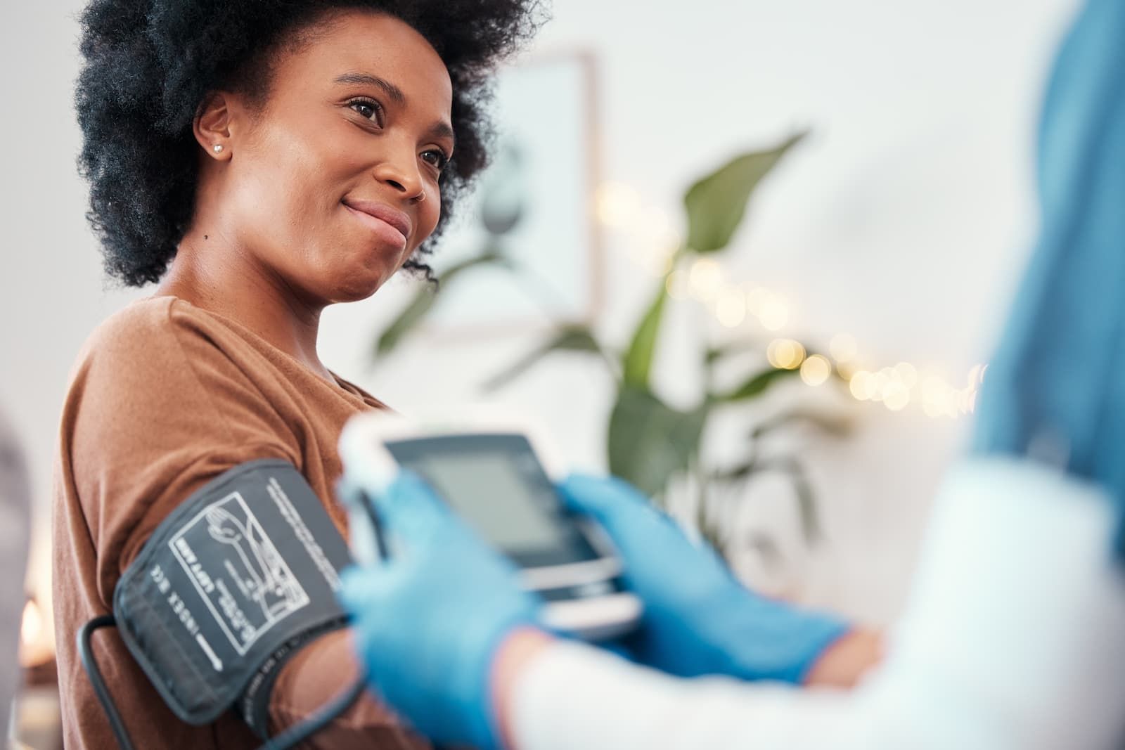 Smiling woman having her blood pressure checked by a healthcare professional wearing blue gloves.