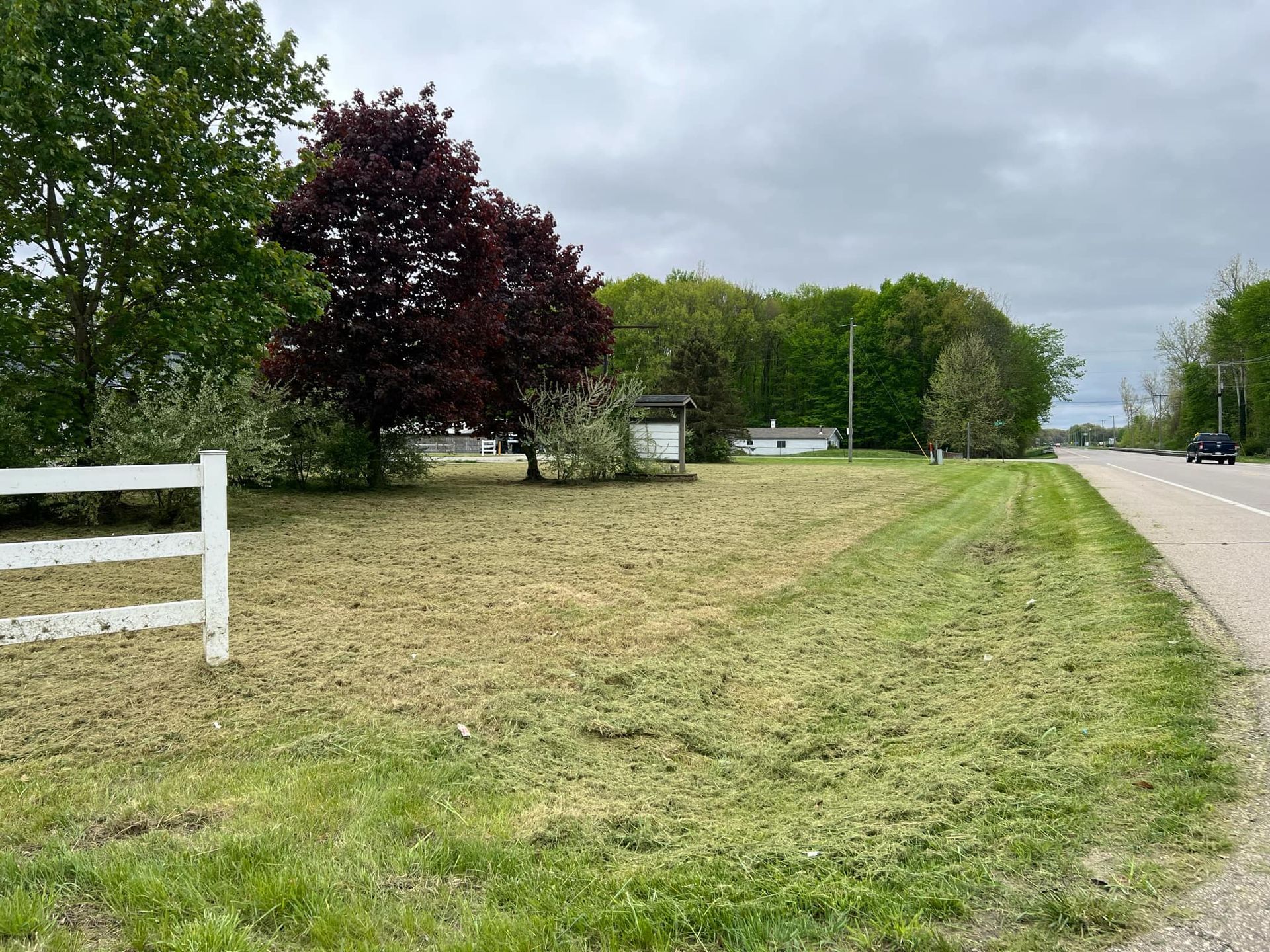 A white fence surrounds a grassy field next to a road.