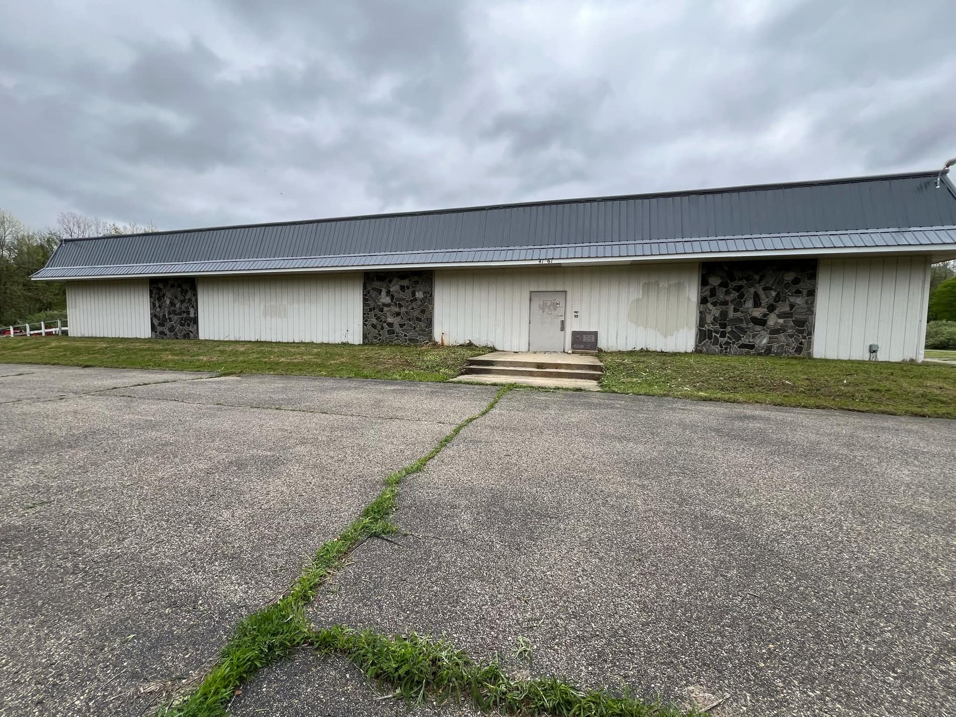 A large white building with a black roof is sitting on top of a gravel lot.