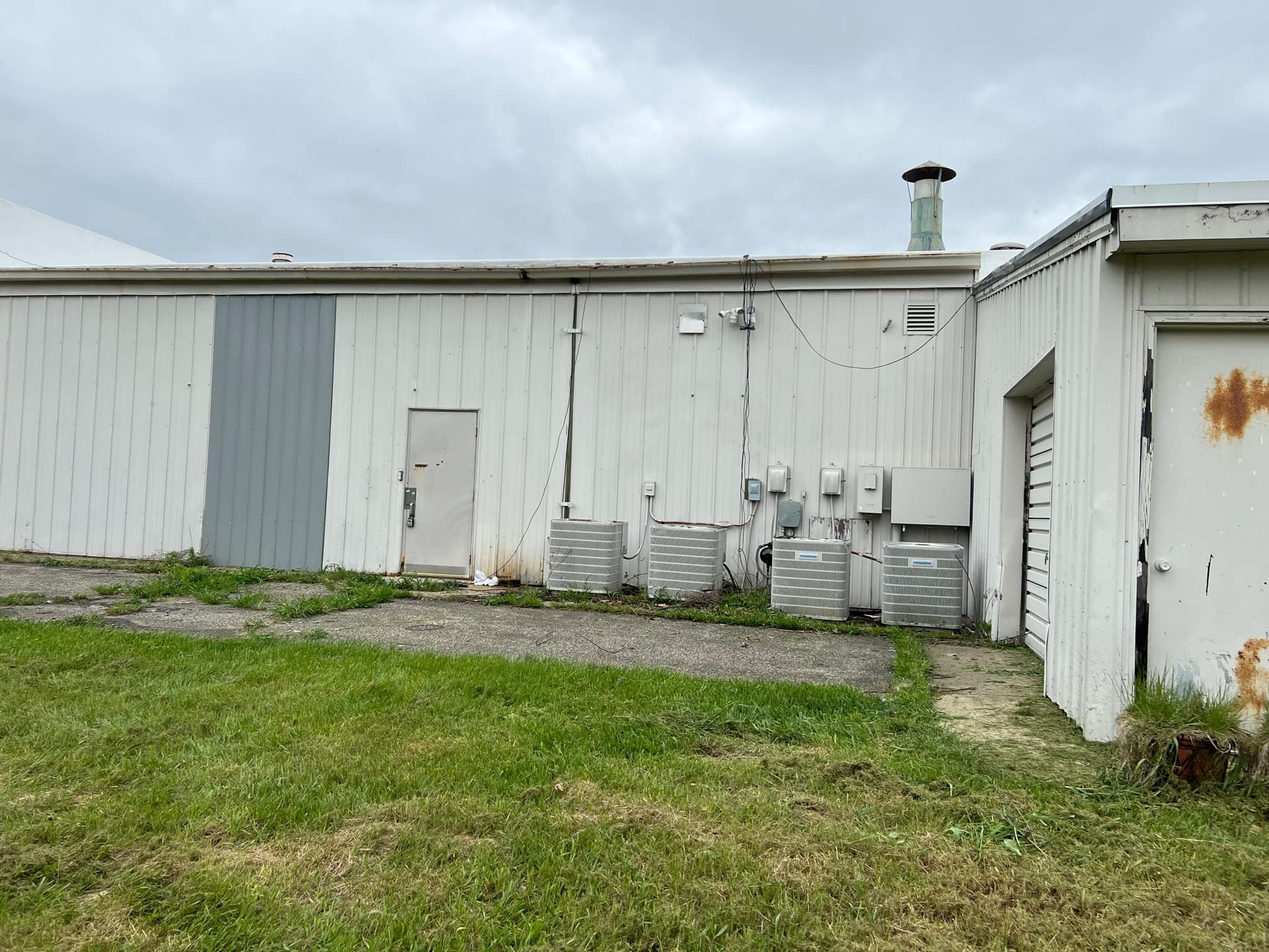 A white building with a gray door is sitting in the middle of a grassy field.