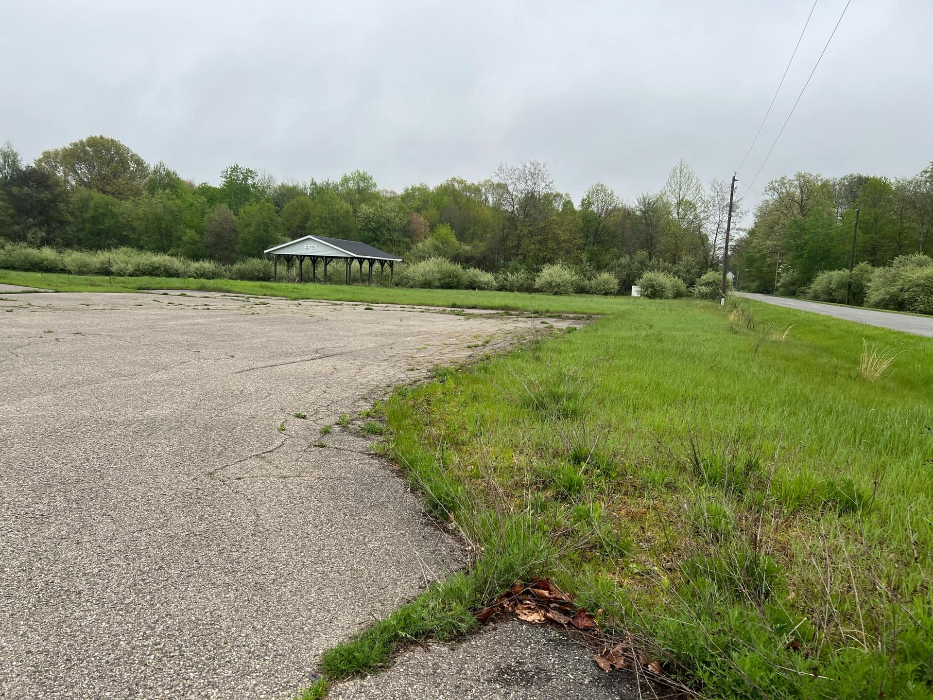 A gravel road going through a grassy field with a shelter in the background.