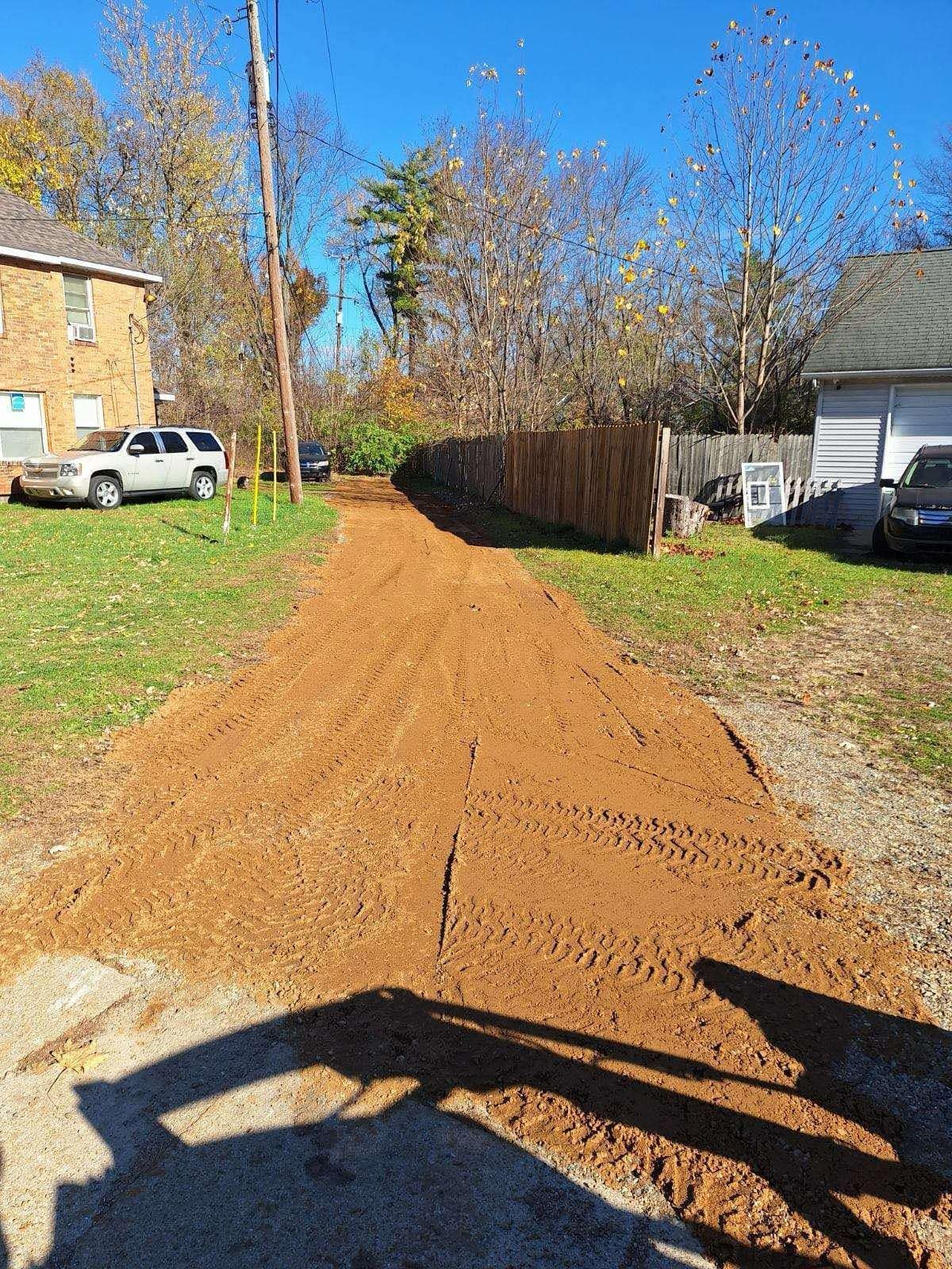 A dirt road with a fence and a house in the background.