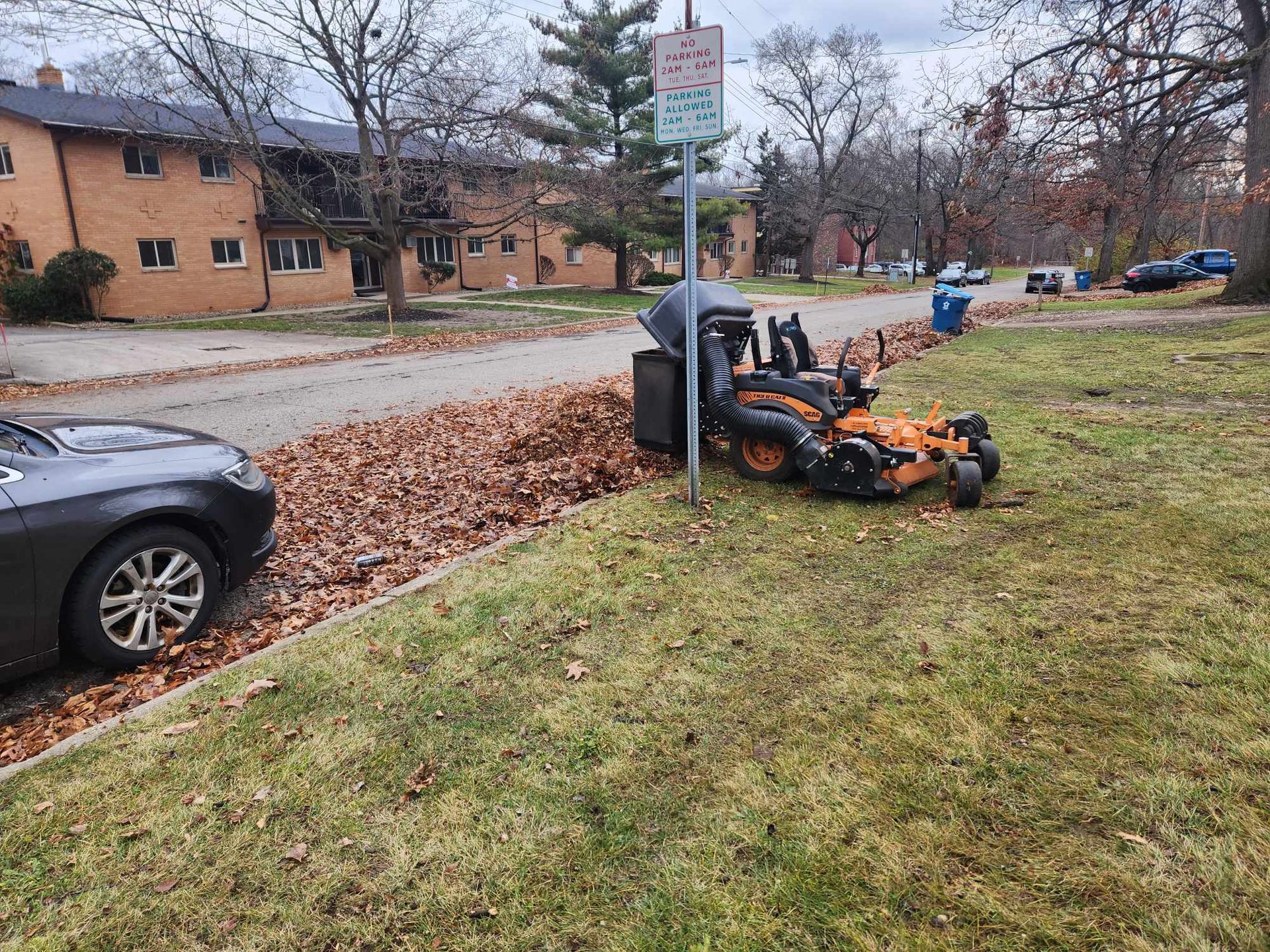A lawn mower is parked on the side of the road next to a car.