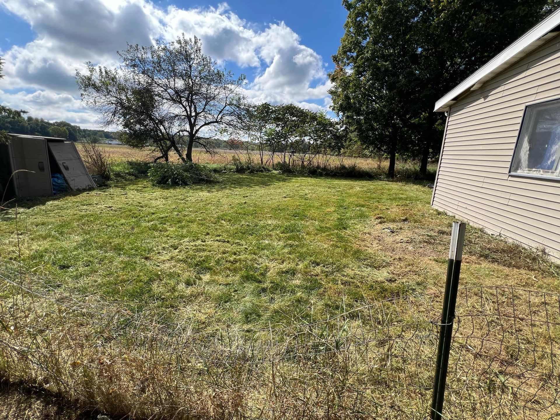 A trailer is parked in a grassy field next to a shed.