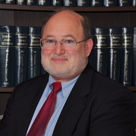 A man in a suit and tie is sitting in front of a shelf of books