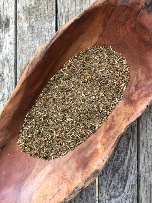 Brown grass seeds fill a wooden bowl set on a weathered wooden surface.