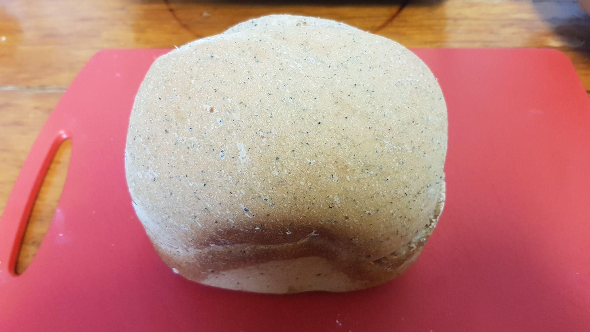 Loaf of bread on a red cutting board. The bread is light brown and has a rough texture.