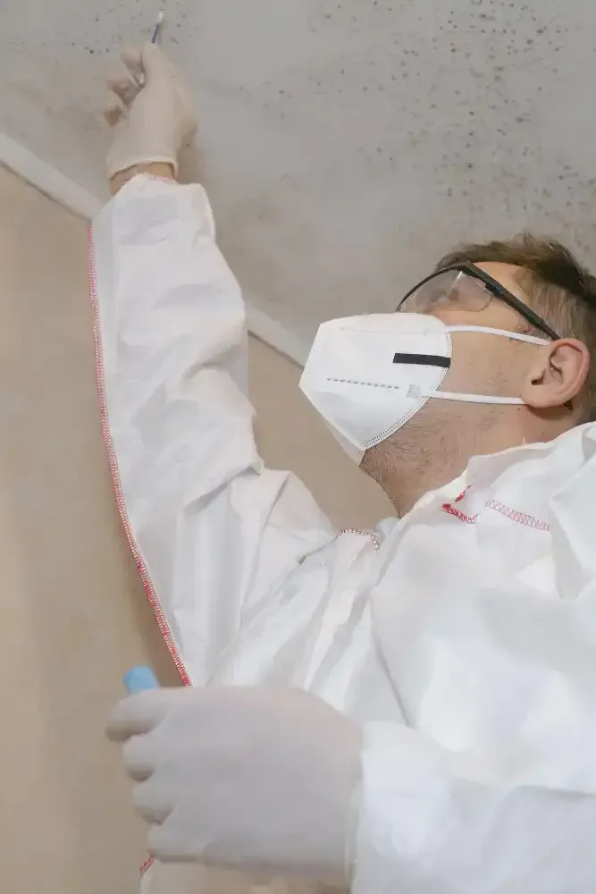 Person in protective gear sprays ceiling, likely for mold remediation.
