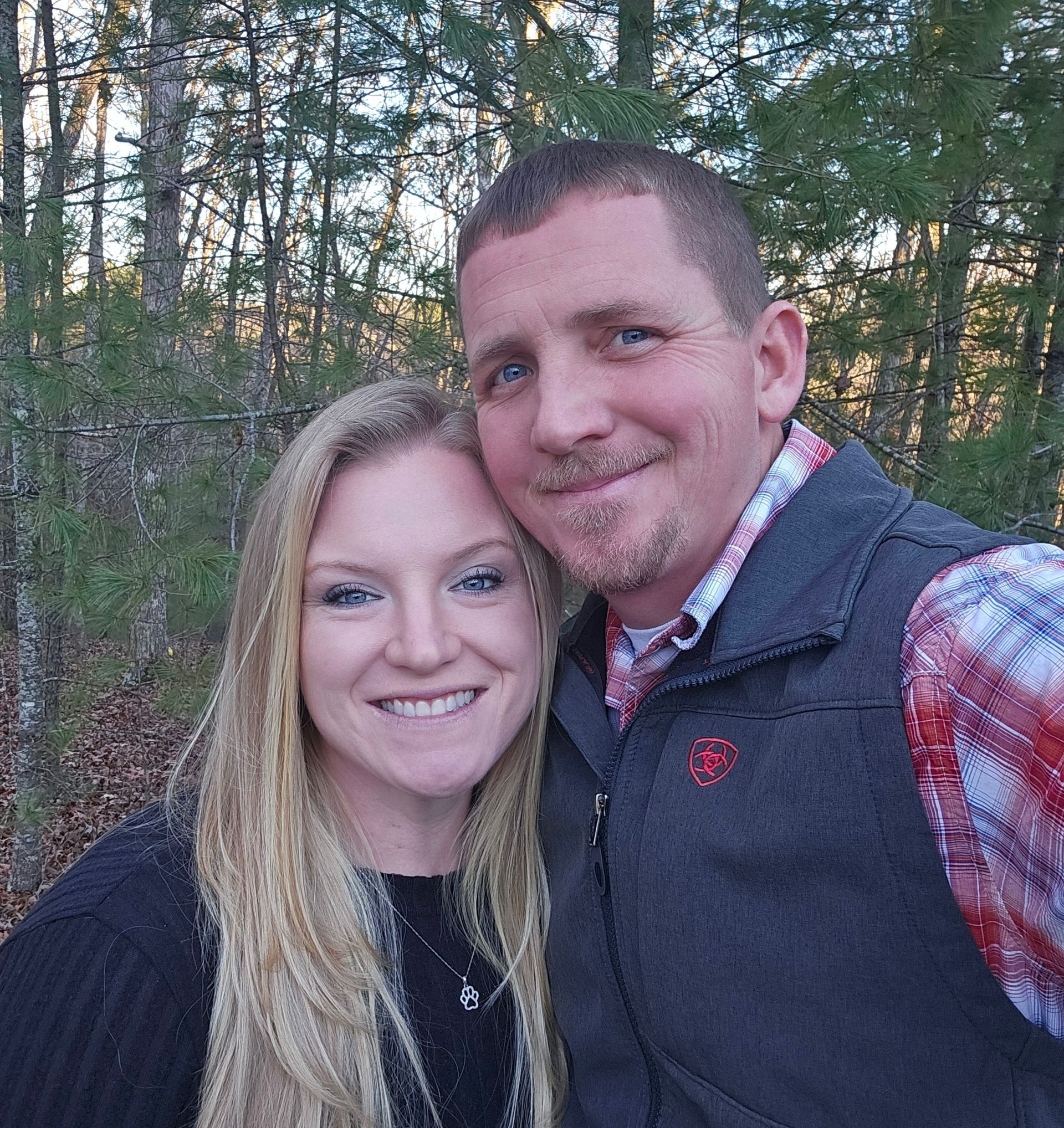 A man and a woman are posing for a picture in the woods.