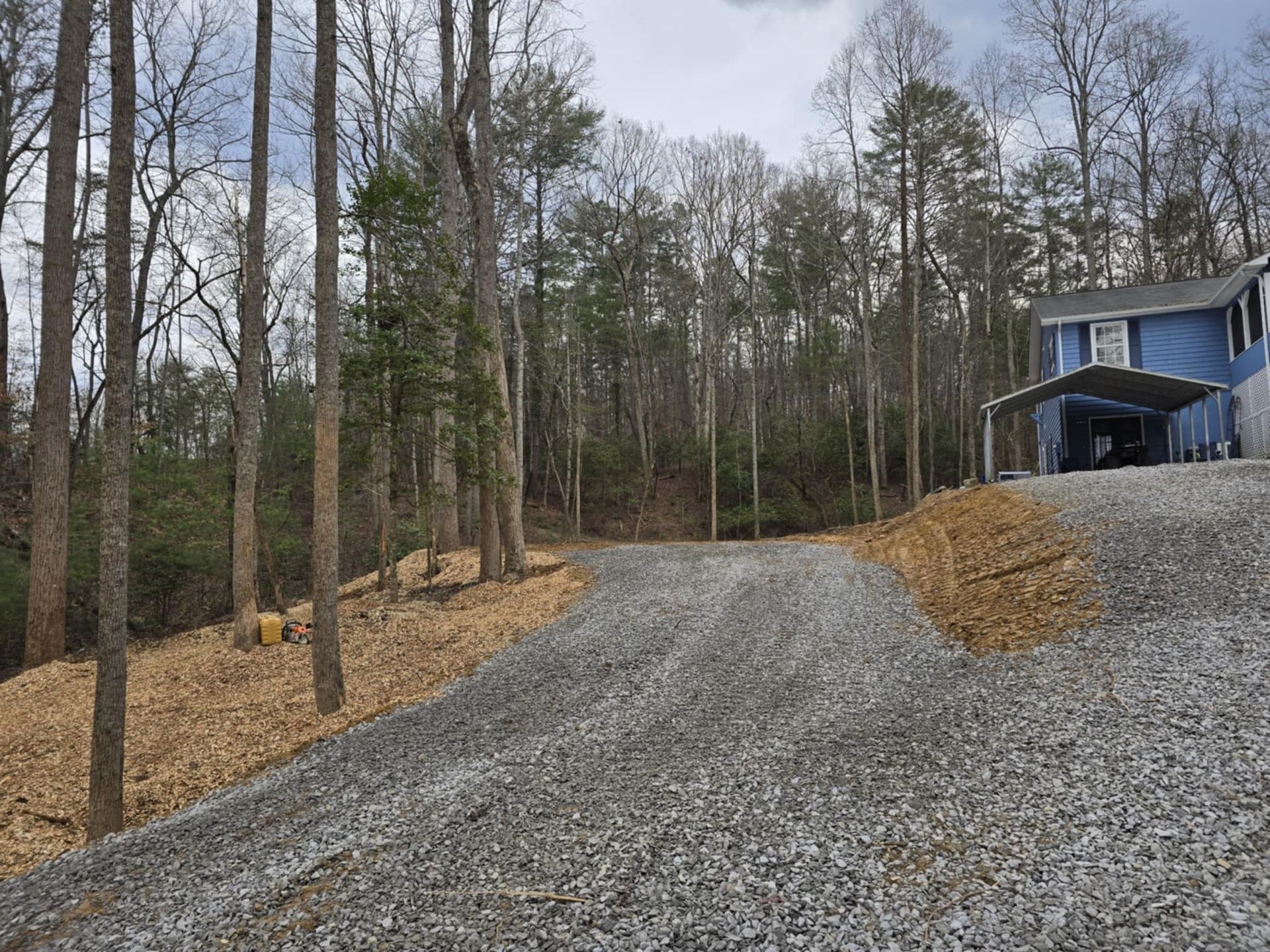 A gravel driveway leading to a blue house in the woods.