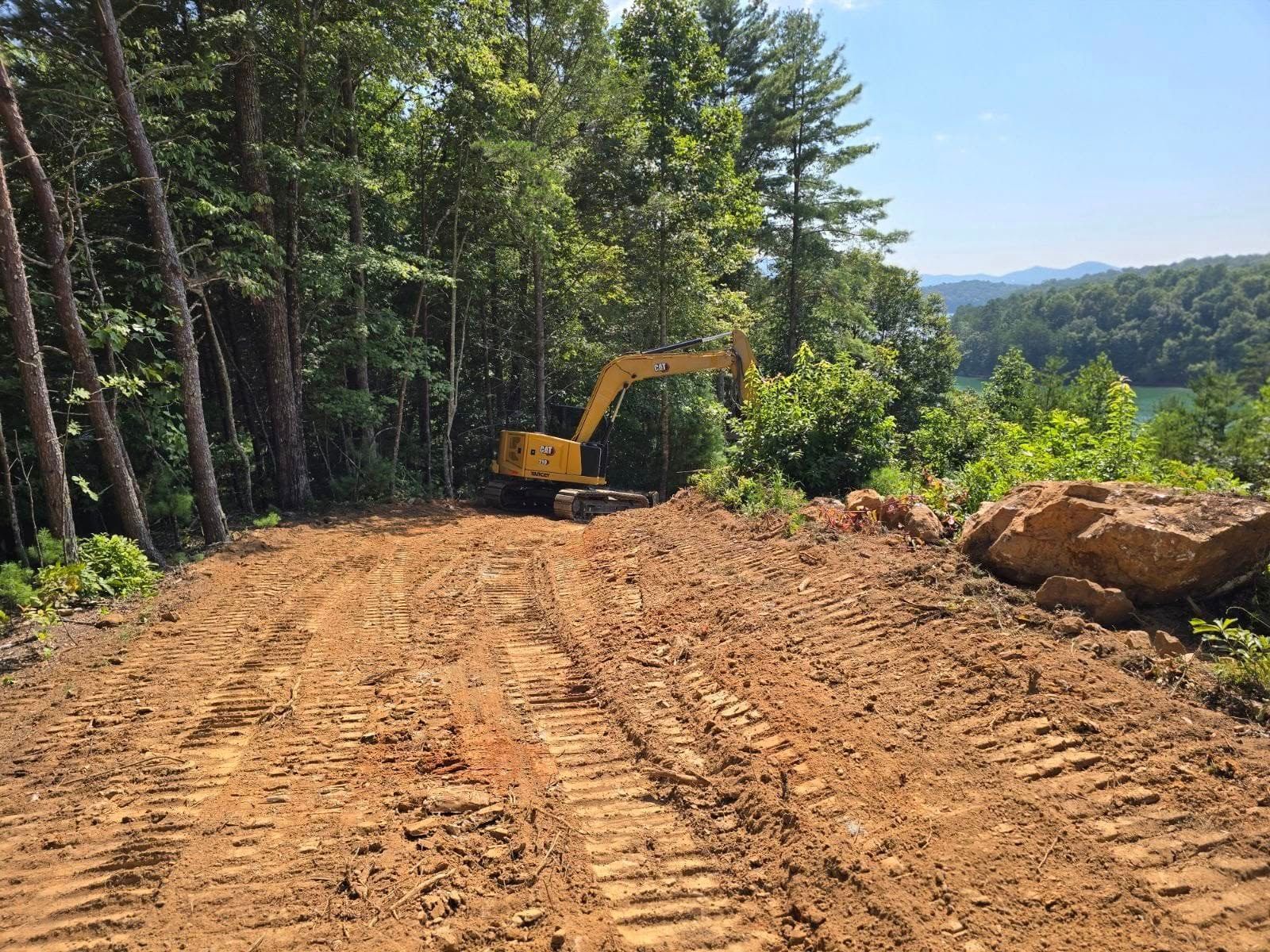 A yellow excavator is driving down a dirt road in the woods.