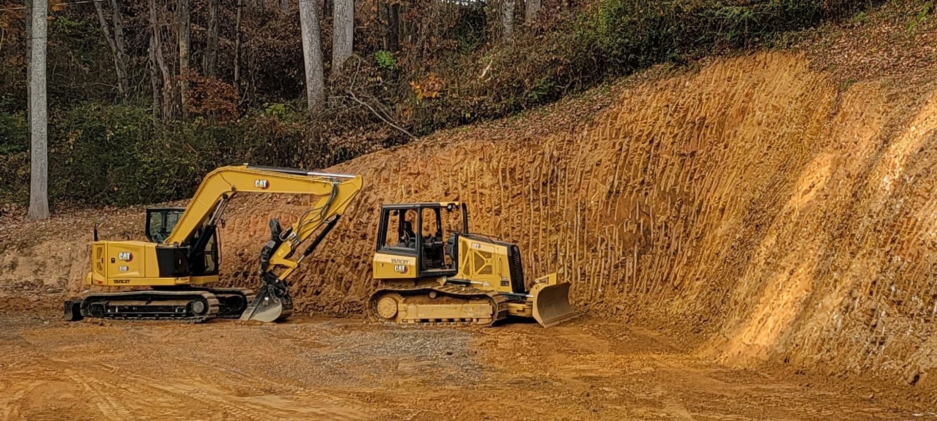 A bulldozer and an excavator are working on a dirt hill.