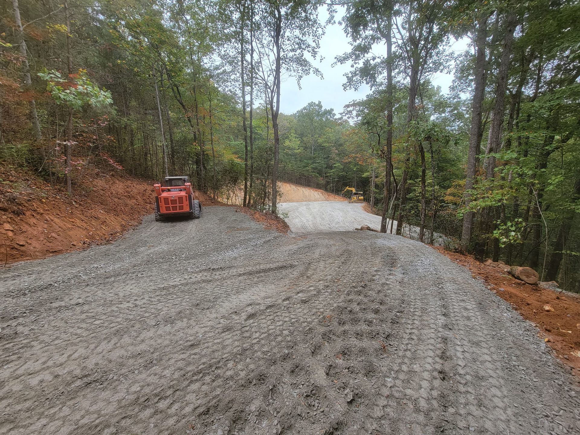 A bulldozer is driving down a dirt road in the woods.