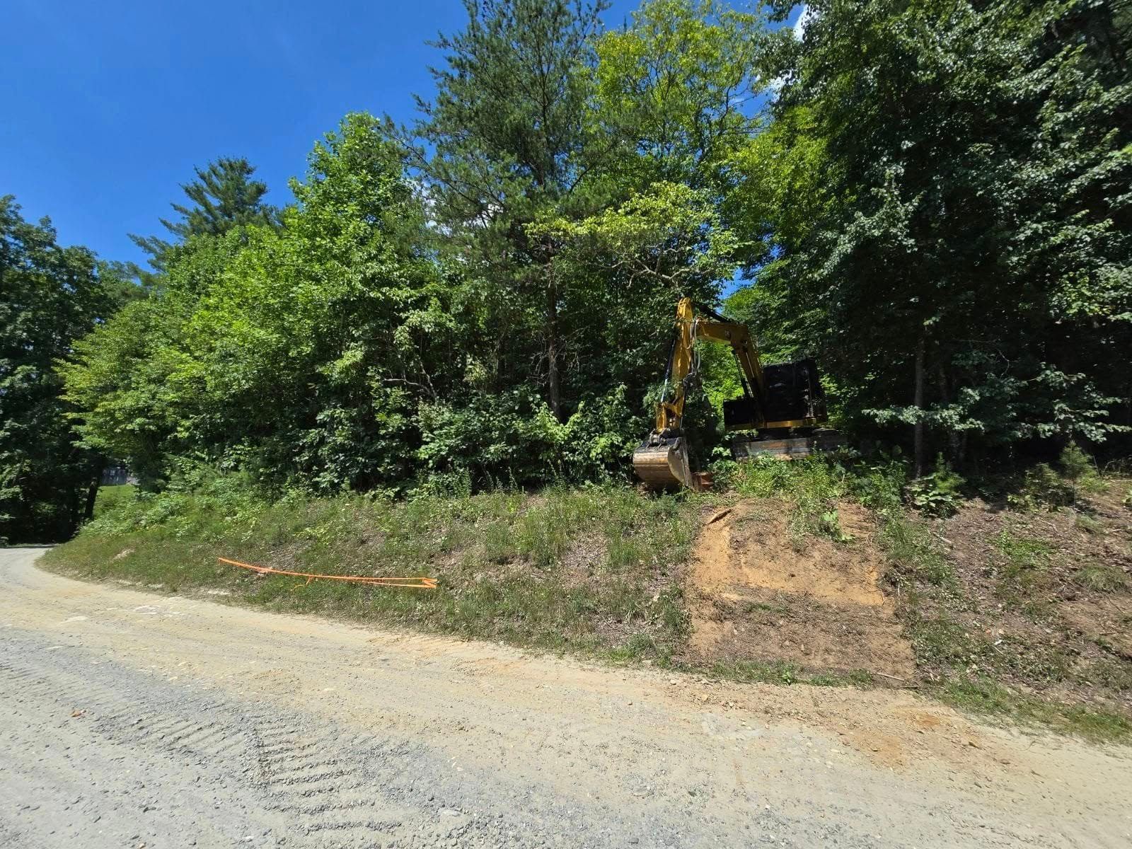 A yellow excavator is sitting on the side of a dirt road.