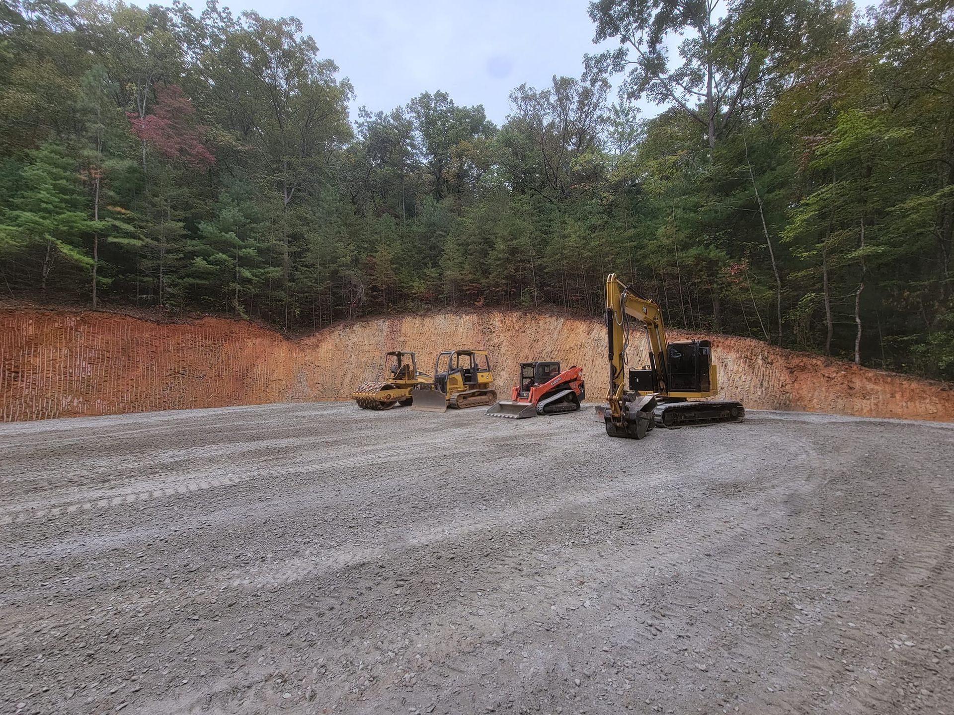 A group of construction vehicles are parked in a gravel lot.