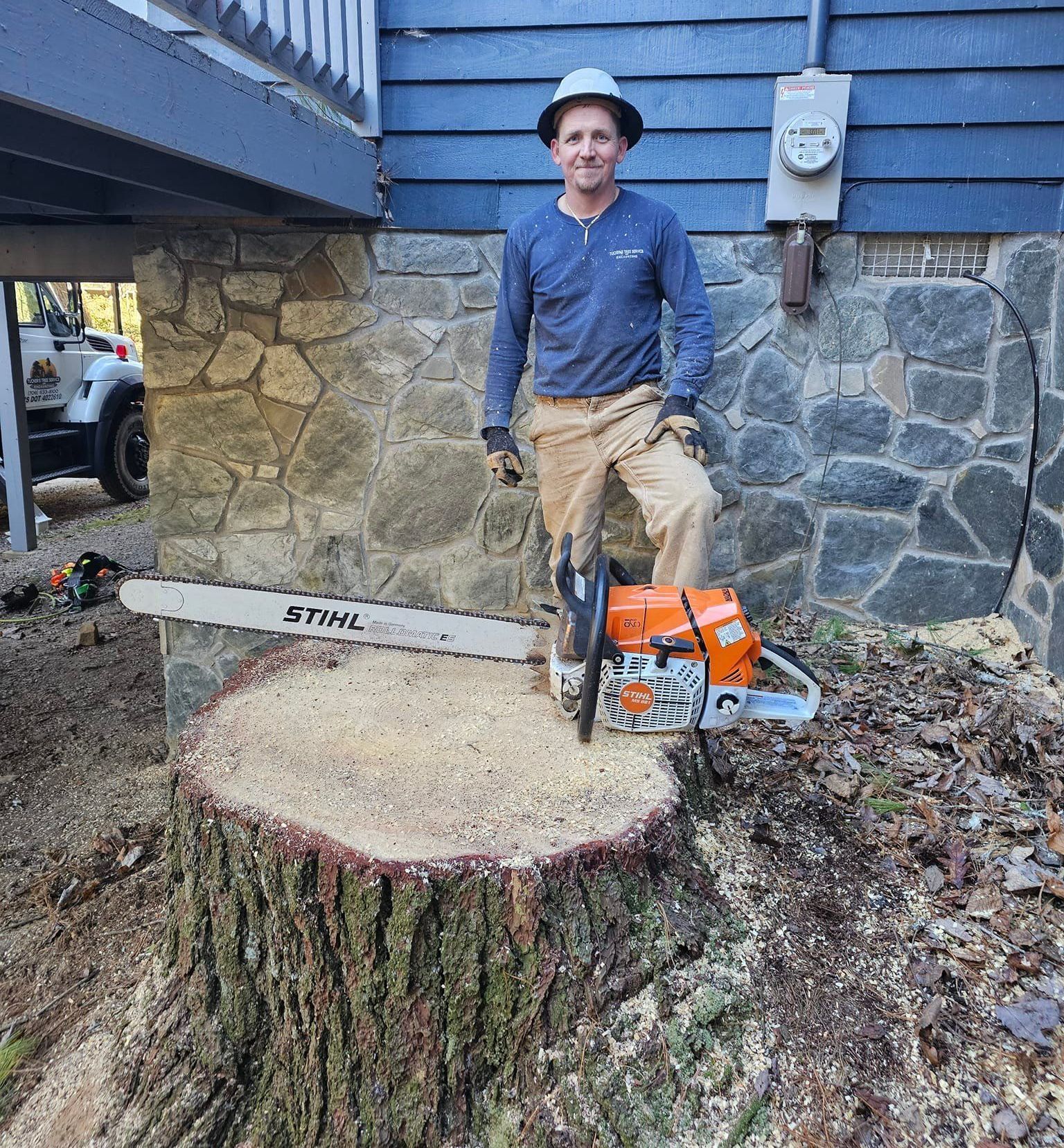 A man is standing next to a chainsaw on a tree stump.