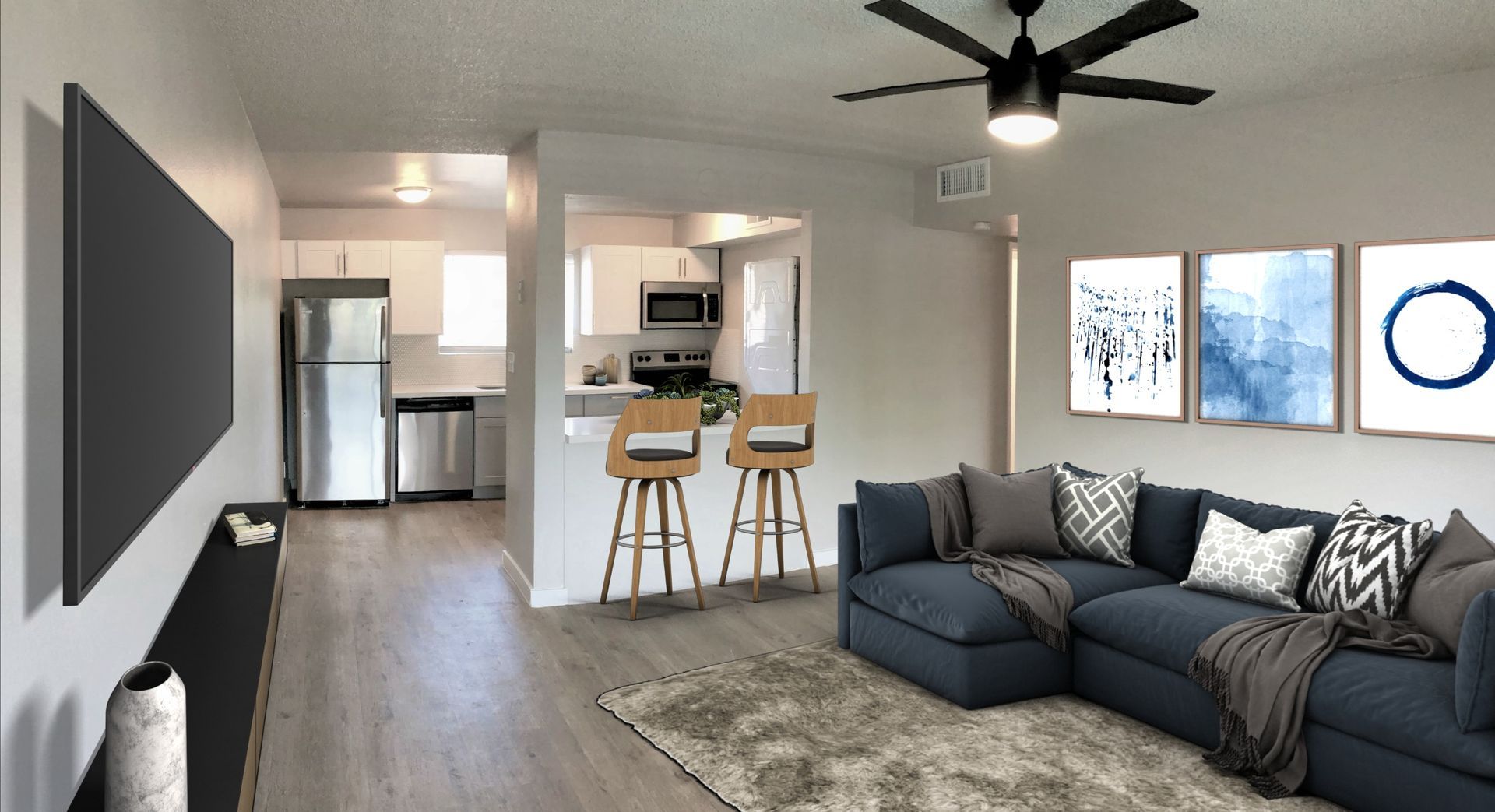 Living room with blue sectional, rug, and kitchen in the background. Artwork on wall.