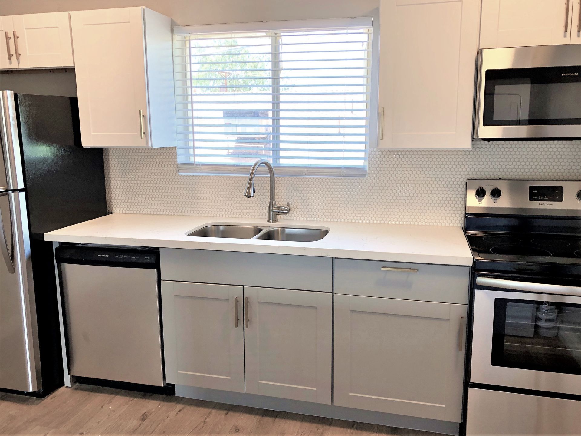 Kitchen with stainless steel appliances, white cabinets, light gray lower cabinets, and a window.